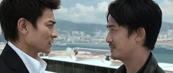Movie still from “Infernal Affairs” (2002), directed by Alan Mak – Two men are looking at one another with a city in the background; Close Up shot, Over the shoulder angle