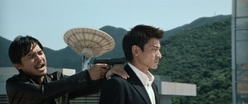 Movie still from “Infernal Affairs” (2002), directed by Alan Mak – A man holding a gun up to his head; Medium shot, Over the shoulder angle