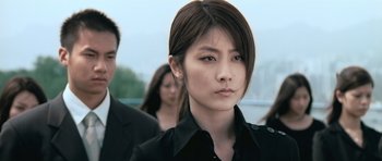 Movie still from “Infernal Affairs” (2002), directed by Alan Mak – A woman in a black shirt is standing in front of a group of people; Close Up shot, Low angle