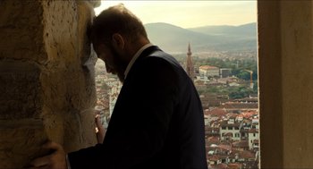 Movie still from “Inferno” (2016), directed by Ron Howard – A man in a suit leaning against a wall; Medium shot, Low angle