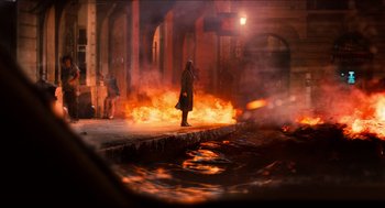 Movie still from “Inferno” (2016), directed by Ron Howard – A person standing in front of a fire on a street; Extreme Wide shot, Over the shoulder angle