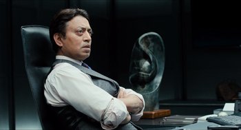 Movie still from “Inferno” (2016), directed by Ron Howard – A person sitting in a chair with his arms crossed; Medium shot, Low angle