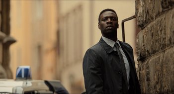Movie still from “Inferno” (2016), directed by Ron Howard – A man wearing a suit and tie standing in front of a building; Medium shot, Low angle