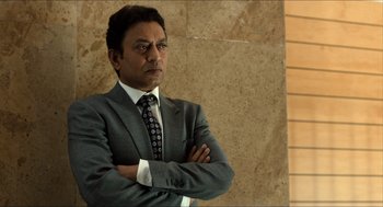 Movie still from “Inferno” (2016), directed by Ron Howard – A man in a suit and tie standing with his arms crossed; Medium shot, Low angle