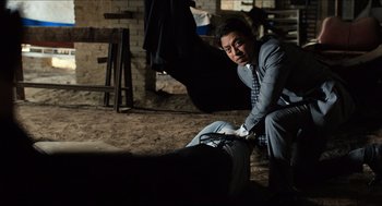 Movie still from “Inferno” (2016), directed by Ron Howard – A man kneeling down next to a chair in a room; Medium shot, High angle