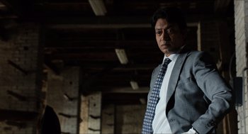 Movie still from “Inferno” (2016), directed by Ron Howard – A man wearing a suit and tie standing in a room; Medium shot, Low angle