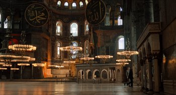 Movie still from “Inferno” (2016), directed by Ron Howard – Two people walking inside a large building with chandeliers; Extreme Wide shot, Low angle