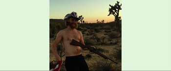 Movie still from “Ingrid Goes West” (2017), directed by Matt Spicer – A shirtless man holding a rifle in the desert at sunset; Medium shot, Low angle