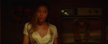 Movie still from “Ingrid Goes West” (2017), directed by Matt Spicer – A woman standing in a dark room wearing a white shirt; Medium shot, Over the shoulder angle