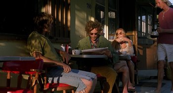 Movie still from “Inherent Vice” (2014), directed by Paul Thomas Anderson – A group of people sitting at a table with food; Medium shot, Low angle