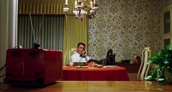 Movie still from “Inherent Vice” (2014), directed by Paul Thomas Anderson – A man sitting at a table with a red table cloth; Wide shot, High angle