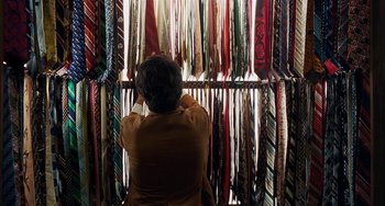 Movie still from “Inherent Vice” (2014), directed by Paul Thomas Anderson – A woman standing in front of a rack filled with ties; Medium shot, Overhead angle