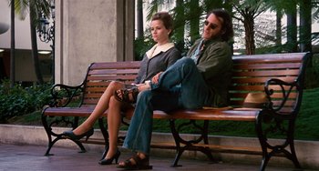 Movie still from “Inherent Vice” (2014), directed by Paul Thomas Anderson – A man and a woman sitting on a wooden bench; Wide shot, Low angle