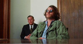 Movie still from “Inherent Vice” (2014), directed by Paul Thomas Anderson – A man sitting in front of another man in front of a mirror; Medium shot, Low angle