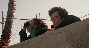 Movie still from “Inherent Vice” (2014), directed by Paul Thomas Anderson – Two men are looking through binoculars at a fence; Close Up shot, Low angle