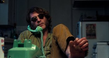 Movie still from “Inherent Vice” (2014), directed by Paul Thomas Anderson – A man sitting on a chair talking on a phone; Close Up shot, Low angle