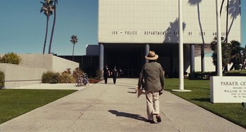 Movie still from “Inherent Vice” (2014), directed by Paul Thomas Anderson – An older man walking down a sidewalk in front of a police station; Wide shot, Low angle