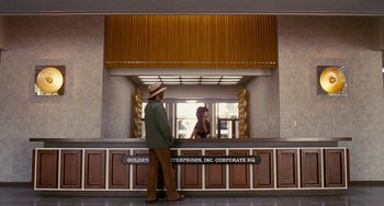 Movie still from “Inherent Vice” (2014), directed by Paul Thomas Anderson – A man and a woman standing in front of a reception desk; Wide shot, Low angle