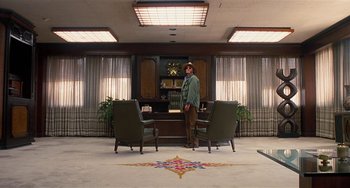 Movie still from “Inherent Vice” (2014), directed by Paul Thomas Anderson – A man standing in front of a desk in a room; Wide shot, Low angle
