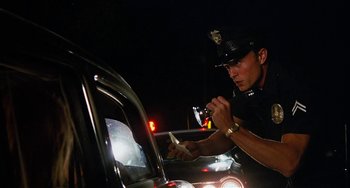 Movie still from “Inherent Vice” (2014), directed by Paul Thomas Anderson – A police officer taking a drink from a glass; Medium shot, Low angle