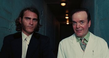 Movie still from “Inherent Vice” (2014), directed by Paul Thomas Anderson – A couple of men standing next to each other in a room; Medium shot, Low angle