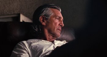 Movie still from “Inherent Vice” (2014), directed by Paul Thomas Anderson – An older man with long gray hair sitting in a chair; Close Up shot, Over the shoulder angle