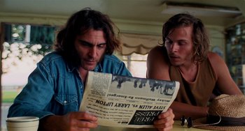 Movie still from “Inherent Vice” (2014), directed by Paul Thomas Anderson – A man reading a newspaper while sitting next to another man; Close Up shot, Low angle