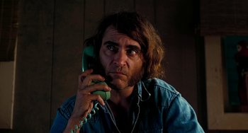 Movie still from “Inherent Vice” (2014), directed by Paul Thomas Anderson – A man holding a phone to his ear while wearing a jean jacket; Close Up shot, Low angle