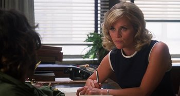 Movie still from “Inherent Vice” (2014), directed by Paul Thomas Anderson – A woman sitting at a table with a pen in her hand; Medium shot, Low angle