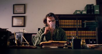 Movie still from “Inherent Vice” (2014), directed by Paul Thomas Anderson – A man sitting at a desk in front of a stack of papers; Medium shot, Low angle
