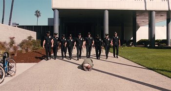 Movie still from “Inherent Vice” (2014), directed by Paul Thomas Anderson – A group of police officers standing in front of a man laying on the ground; Extreme Wide shot, High angle