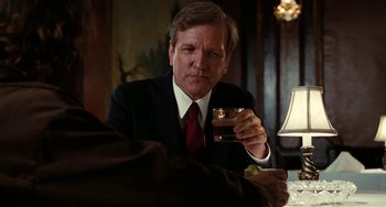 Movie still from “Inherent Vice” (2014), directed by Paul Thomas Anderson – A man sitting at a table holding a glass of wine; Close Up shot, Over the shoulder angle