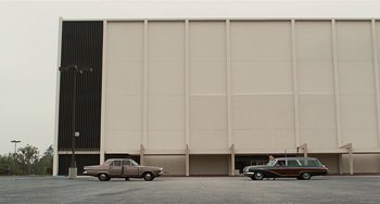 Movie still from “Inherent Vice” (2014), directed by Paul Thomas Anderson – A couple of cars parked in front of a large building; Extreme Wide shot, Low angle