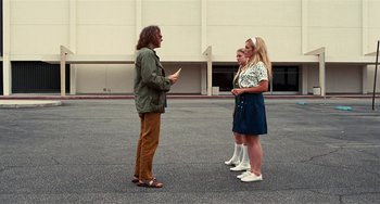 Movie still from “Inherent Vice” (2014), directed by Paul Thomas Anderson – A group of people standing in a parking lot; Wide shot, Over the shoulder angle