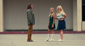 Movie still from “Inherent Vice” (2014), directed by Paul Thomas Anderson – A man and two women standing next to each other on the street; Wide shot, Over the shoulder angle