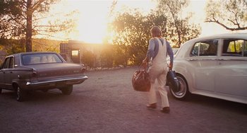 Movie still from “Inherent Vice” (2014), directed by Paul Thomas Anderson – A man carrying a bag of luggage walks down the street; Wide shot, Low angle