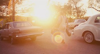 Movie still from “Inherent Vice” (2014), directed by Paul Thomas Anderson – A person walking in a parking lot near some parked cars; Wide shot, Low angle