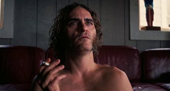 Movie still from “Inherent Vice” (2014), directed by Paul Thomas Anderson – A man sitting on a couch with a cigarette in his mouth; Close Up shot, Low angle