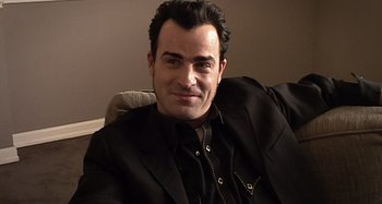 Movie still from “Inland Empire” (2006), directed by David Lynch – A person sitting on a couch wearing a suit; Close Up shot, High angle