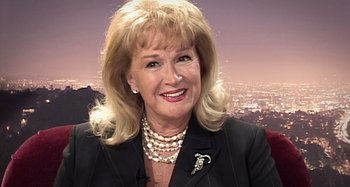 Movie still from “Inland Empire” (2006), directed by David Lynch – A person wearing a suit and pearl necklace; Close Up shot, High angle