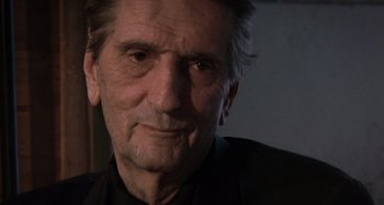Movie still from “Inland Empire” (2006), directed by David Lynch – An older man in a black shirt is looking at the camera; Close Up shot, Low angle
