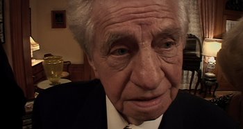 Movie still from “Inland Empire” (2006), directed by David Lynch – An older man wearing a suit and tie; Extreme Close Up shot, High angle