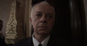 Movie still from “Inland Empire” (2006), directed by David Lynch – An older man wearing a suit and tie; Close Up shot, Low angle