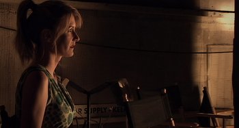 Movie still from “Inland Empire” (2006), directed by David Lynch – A woman standing next to a desk in a dark room; Close Up shot, Low angle