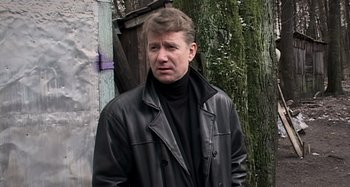 Movie still from “Inland Empire” (2006), directed by David Lynch – A man in a black jacket standing next to a tree; Close Up shot, Low angle
