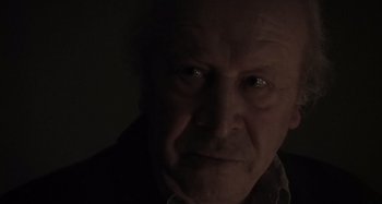 Movie still from “Inland Empire” (2006), directed by David Lynch – An old man with a serious look on his face in the dark; Close Up shot, Low angle