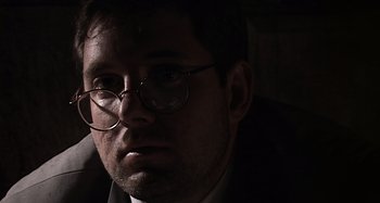 Movie still from “Inland Empire” (2006), directed by David Lynch – A person wearing glasses and a suit; Close Up shot, Low angle