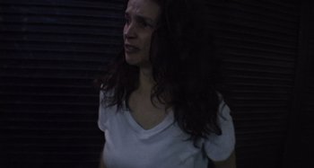 Movie still from “Inland Empire” (2006), directed by David Lynch – A woman in a white t - shirt is standing in a dark room; Close Up shot, Low angle