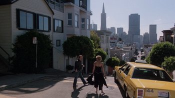 Movie still from “Innerspace” (1987), directed by Joe Dante – Two people walking down a street with a yellow taxi cab in the background; Wide shot, High angle