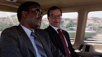 Movie still from “Innerspace” (1987), directed by Joe Dante – Two men sitting in a car wearing suits and ties; Close Up shot, Low angle